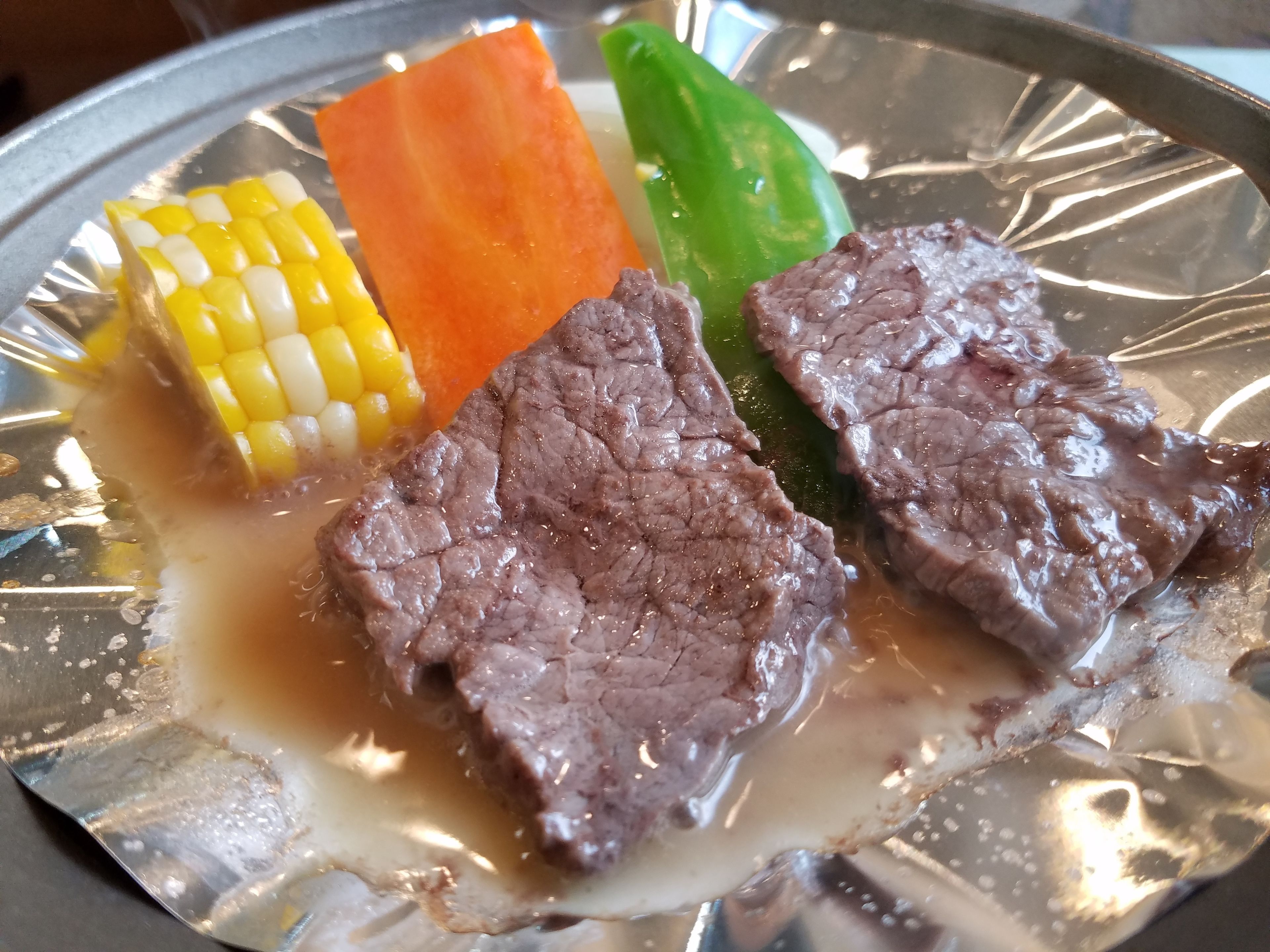 A plate with slices of beef, corn on the cob, carrot, and green bell pepper.