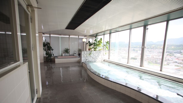 Un espacio interior amplio con una piscina de vidrio curvo, ventanas grandes que ofrecen vista a la ciudad y plantas en macetas.