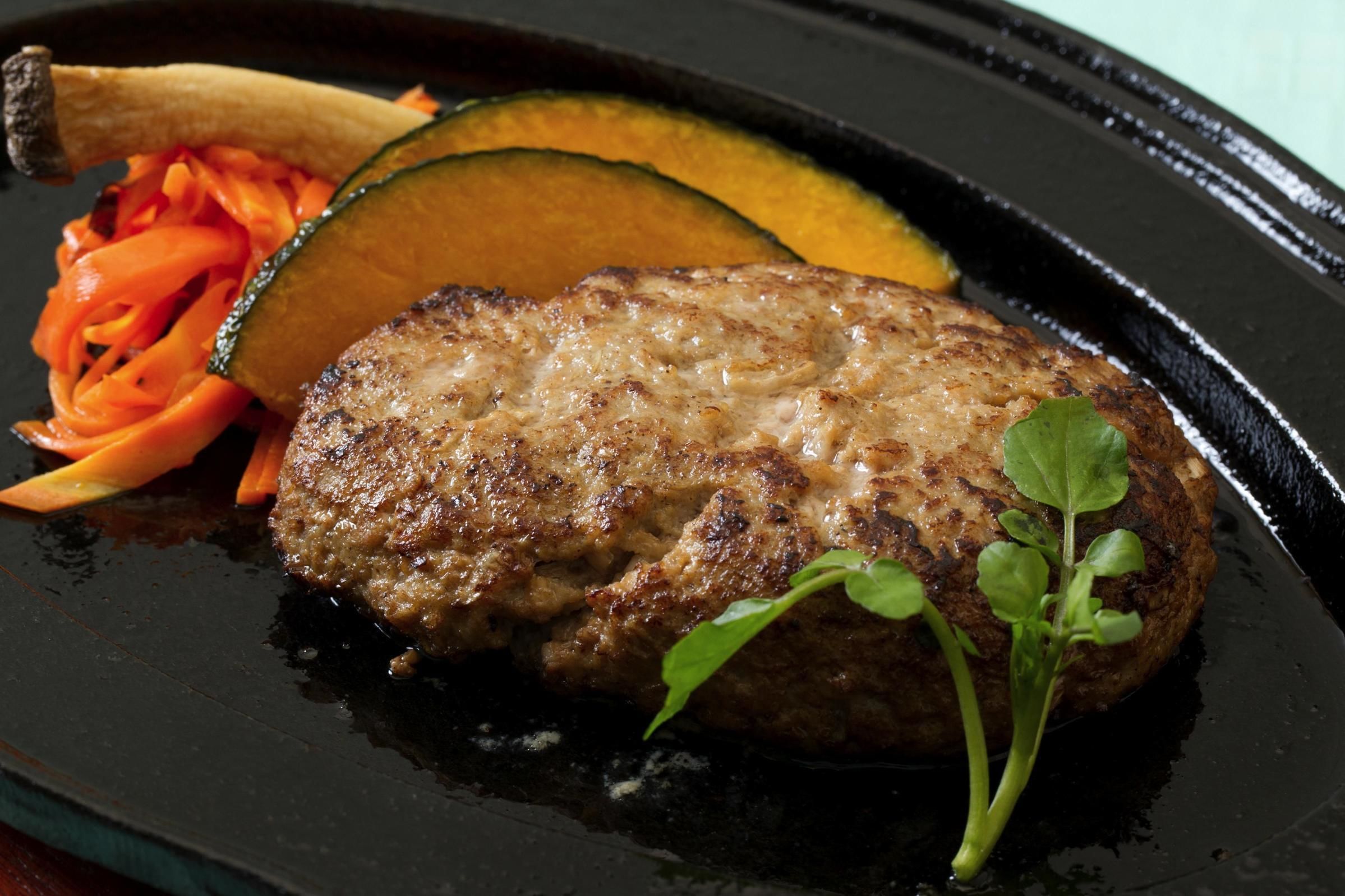 A steak with a side of carrots and zucchini on a black plate.