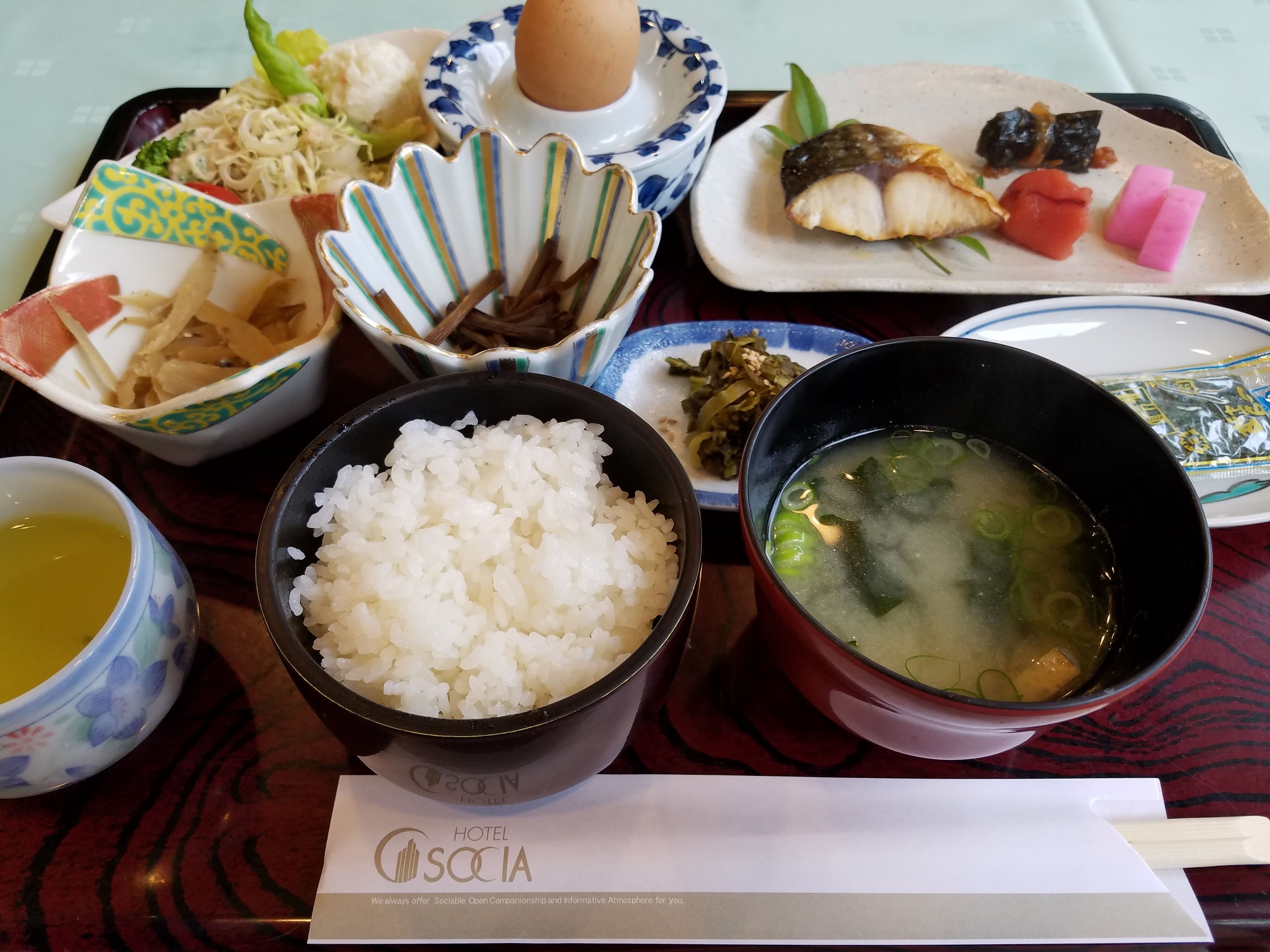 A variety of Japanese dishes including rice, soup, and sashimi on a tray.
