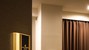 Habitación de hotel con puerta moderna, cama con colcha estampada, mesita de noche con lámpara y teléfono instalado en la pared.