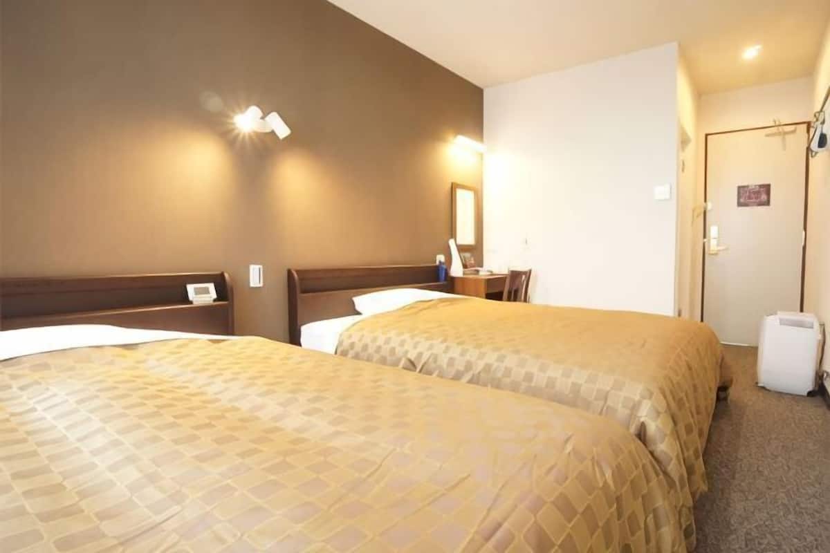 Une chambre d’hôtel avec deux lits, un bureau, une chaise, un miroir et une porte.