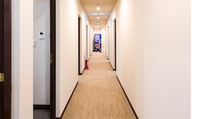 Un pasillo de hotel con pisos alfombrados, paredes blancas y puertas a ambos lados.