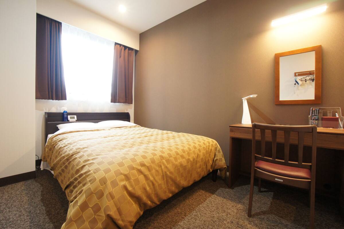 Une chambre d’hôtel avec un lit, un bureau, une chaise, une lampe et un tableau encadré au mur.
