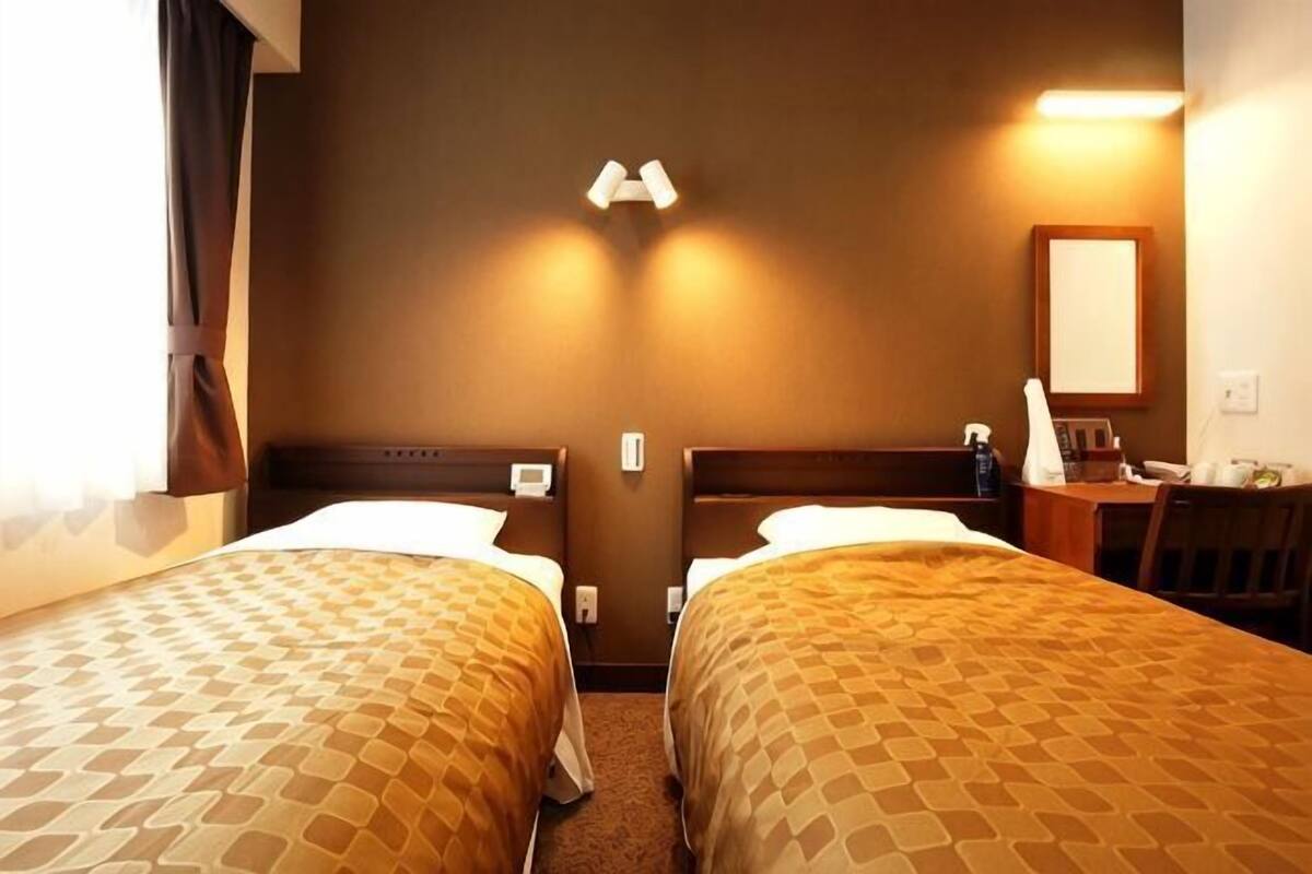 Une chambre d’hôtel avec deux lits, un bureau, une chaise, un miroir et une table de chevet.