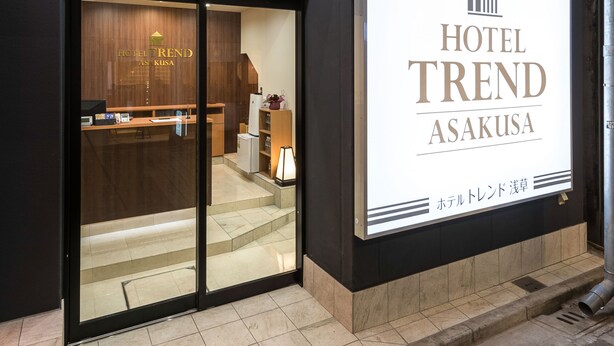 Entrada de hotel con una recepción, un cartel con el nombre del hotel y una escalera que da al interior.
