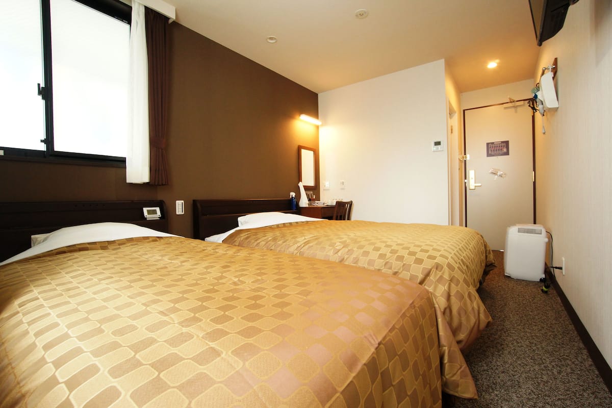 Une chambre d’hôtel avec deux lits, une table de chevet, une lampe, un miroir, une porte et un petit radiateur.