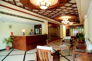 Un vestíbulo de hotel con mostrador de recepción, zona de estar y techo decorativo.