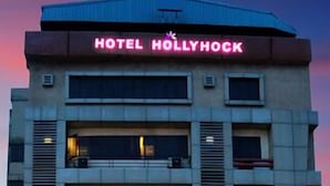 Ein mehrstöckiges Gebäude mit einem Schild, auf dem „HOTEL HOLLYHOCK“ steht, und einem Eingang.