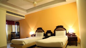 Ein Hotelzimmer mit zwei Einzelbetten, einem Nachttisch mit Lampe, einem Sessel und einem Fenster mit Vorhängen.