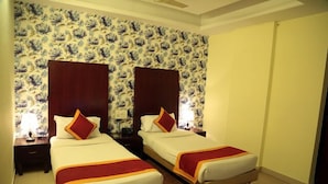 Ein Hotelzimmer mit zwei Betten, floralem Wandpapier, Holz-Kopfteilen und rotem Akzent an den Betten.