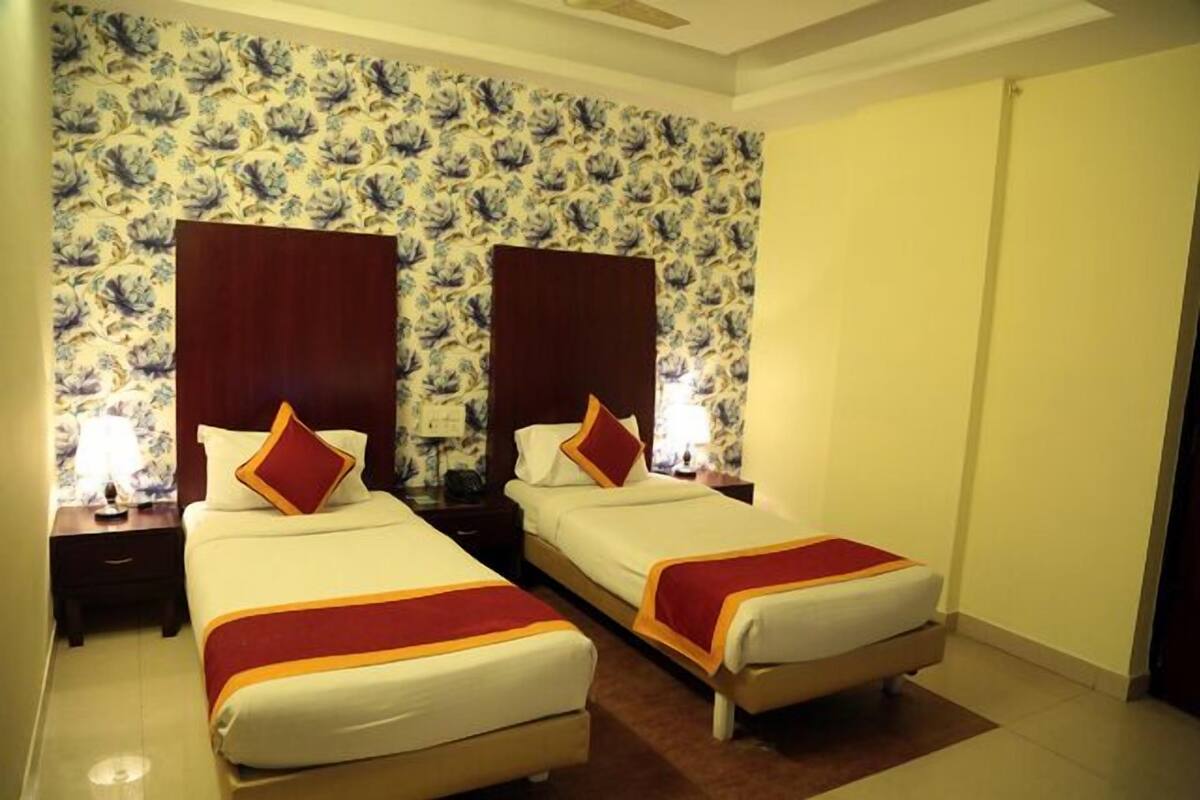 A hotel room with two beds, floral wallpaper, wooden headboards, and a red accent on the beds.
