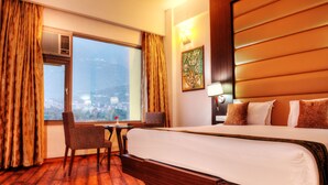 Habitación de hotel con una cama grande, un escritorio con silla, una ventana con cortinas y vistas a la ciudad.
