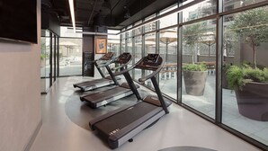Une salle de sport moderne équipée de tapis de course, dotée de grandes fenêtres et agrémentée de plantes d’intérieur.