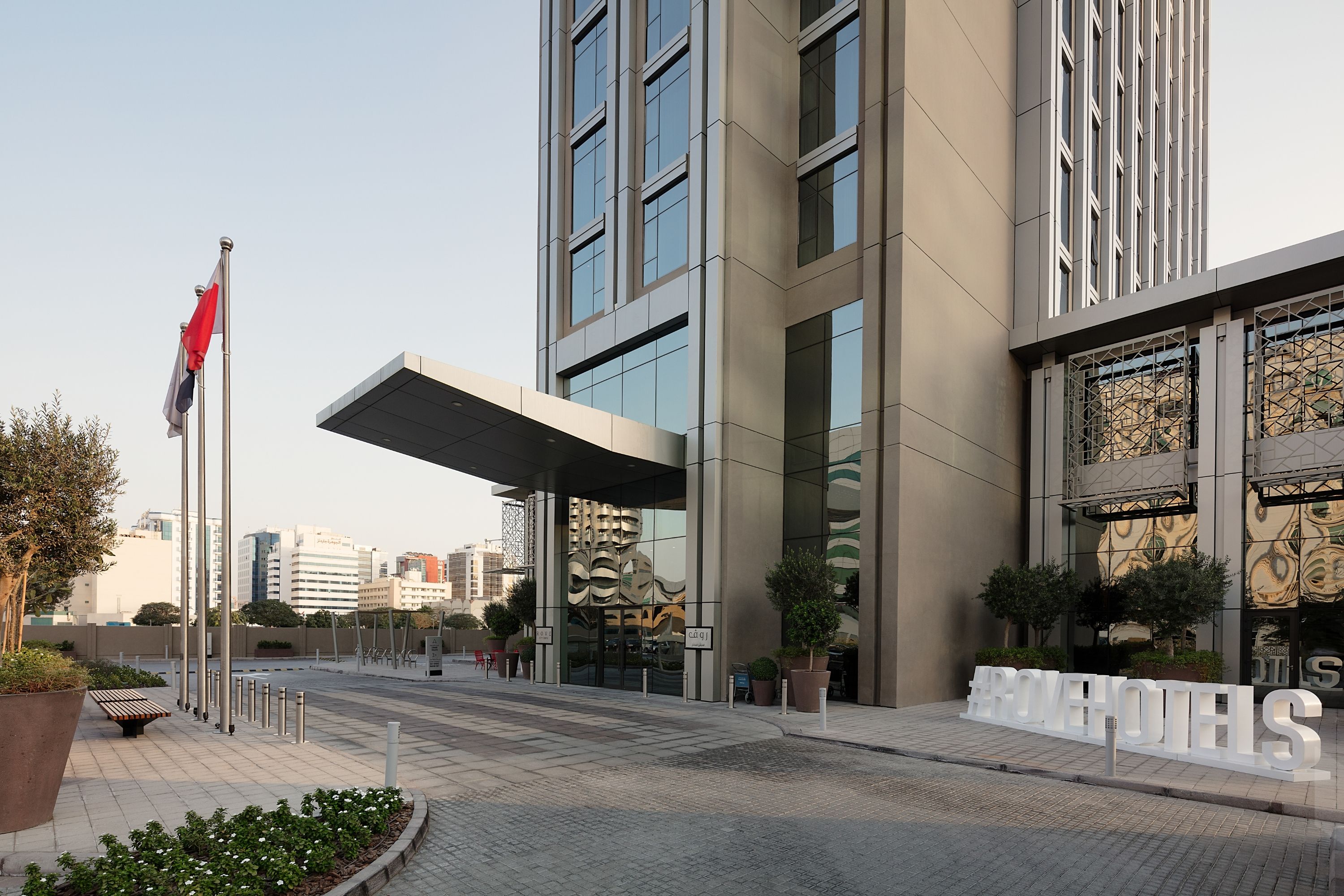 Una entrada de hotel moderna con un corredor cubierto, ventanas amplias y un cartel que dice 'AROVEH HOTELS'.