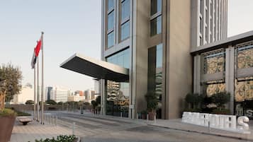 Una entrada de hotel moderna con un corredor cubierto, ventanas amplias y un cartel que dice 'AROVEH HOTELS'.