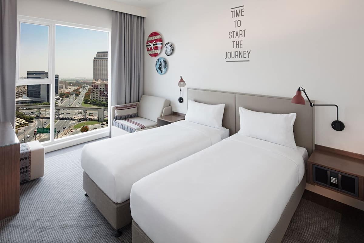 A hotel room with two beds, a view of the city, a desk, and a chair.