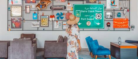 A modern interior with a large wall decorated with various items and a sign indicating directions to Deira Clock Tower and Port Saeed.