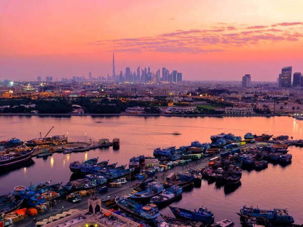 A harbor with numerous boats docked, a city skyline in the background, and a sunset sky. - Rove City Centre, Deira (Dubai)