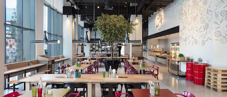 A modern cafe interior with multiple tables and chairs, a large hanging plant, and a wall with utensil illustrations.