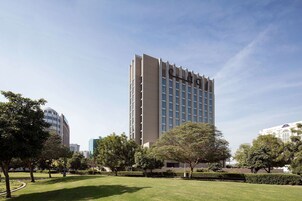 A modern hotel with a central tower and surrounding greenery.
