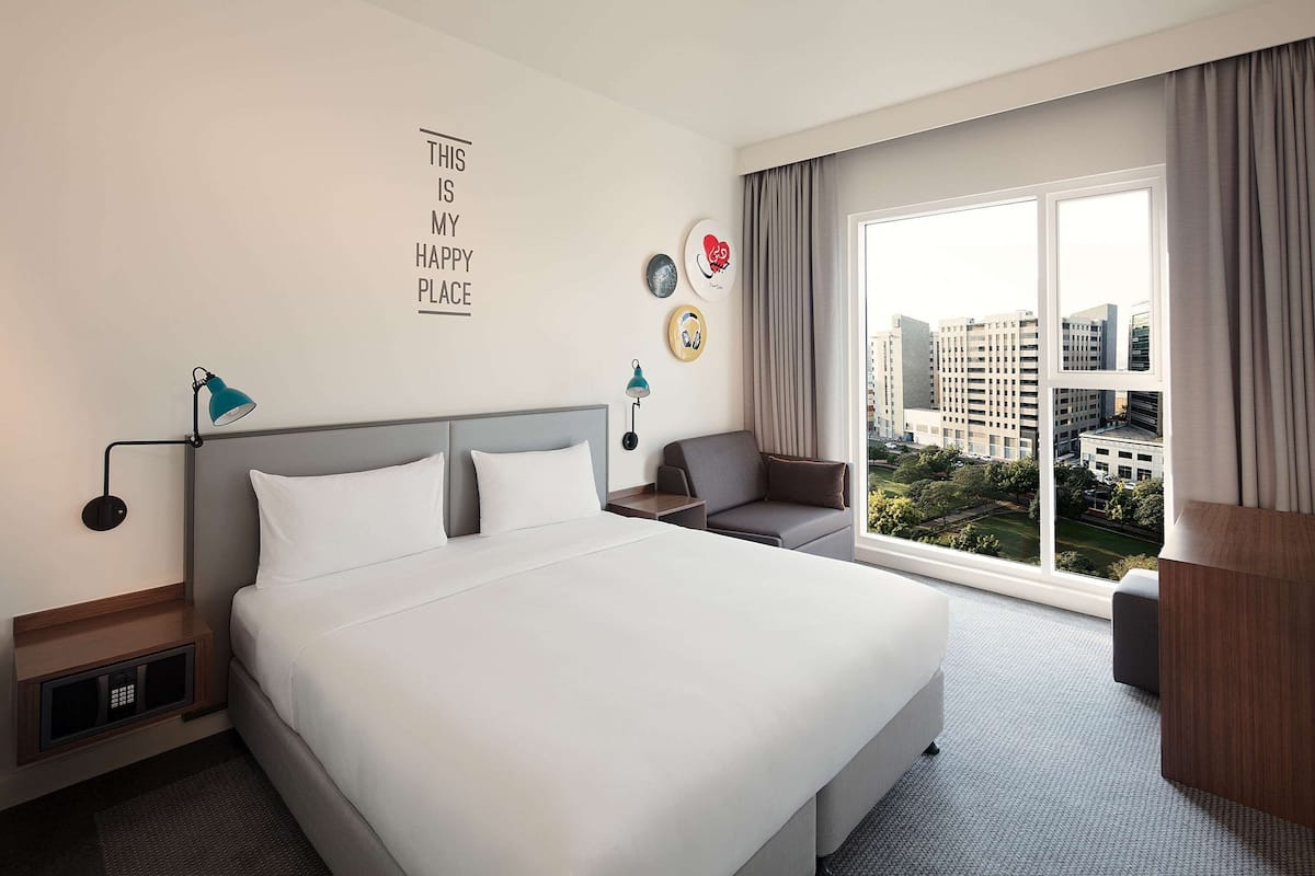 A hotel room with a large bed, a sofa, a desk, and a view of the cityscape.