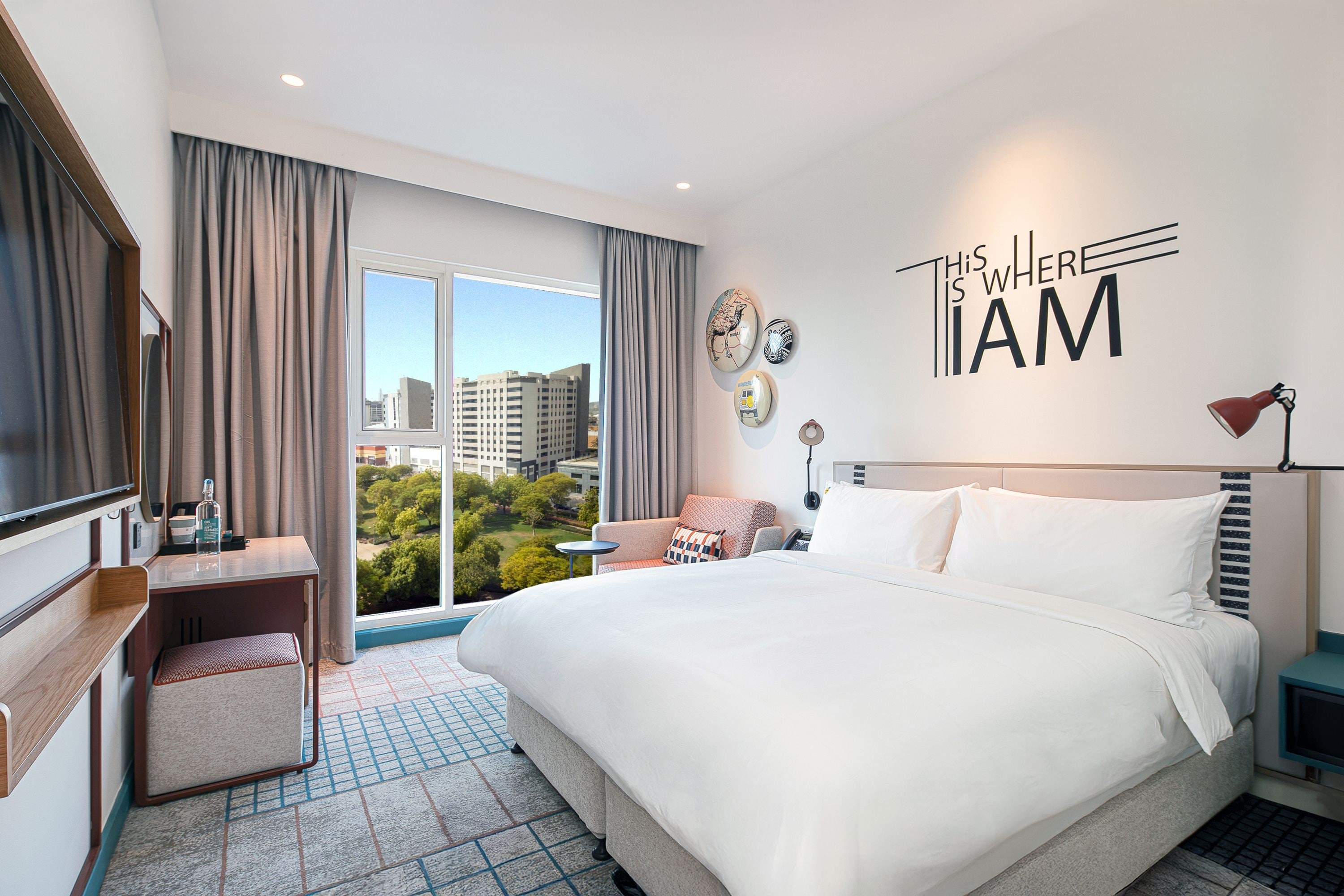 Une chambre d’hôtel avec un grand lit, un bureau, une chaise, une télévision et une vue sur le paysage urbain.