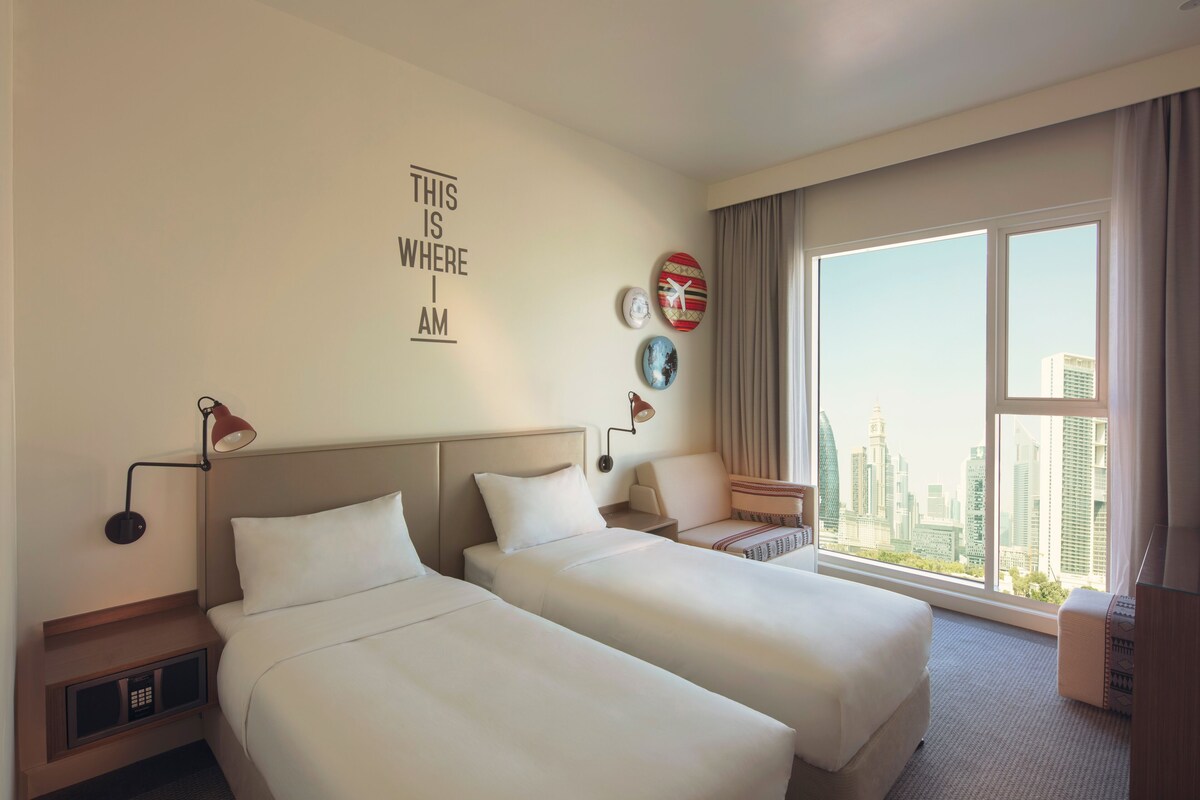 A hotel room with two beds, a city view, a wall clock, and a motivational quote.