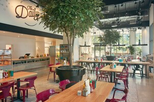 A modern restaurant interior with multiple dining tables and chairs, a large potted tree, and a wall with the restaurant's name.