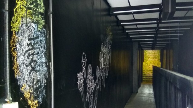 Een gang met graffiti op de muren, metalen leuningen en een betegelde vloer.