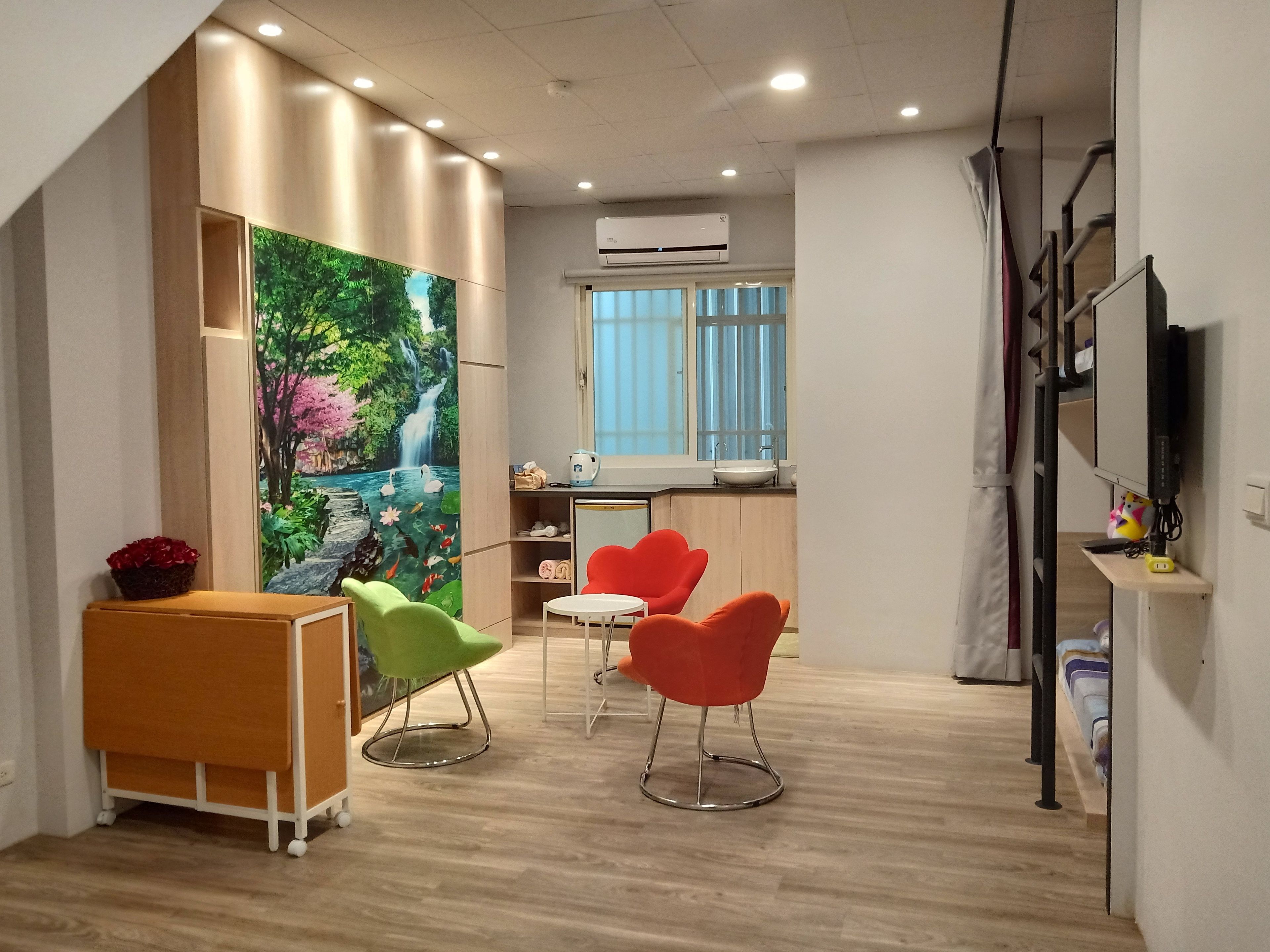 A modern room with a wooden floor, a painting of a waterfall, a small kitchenette, and two chairs.