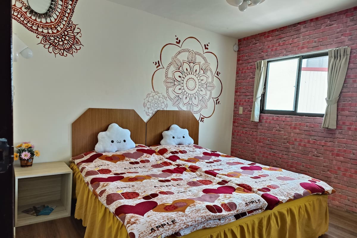Un dormitorio con cabecera de madera, cama con colcha colorida con motivos de manzanas, un adorno de pared y una pared de ladrillo.