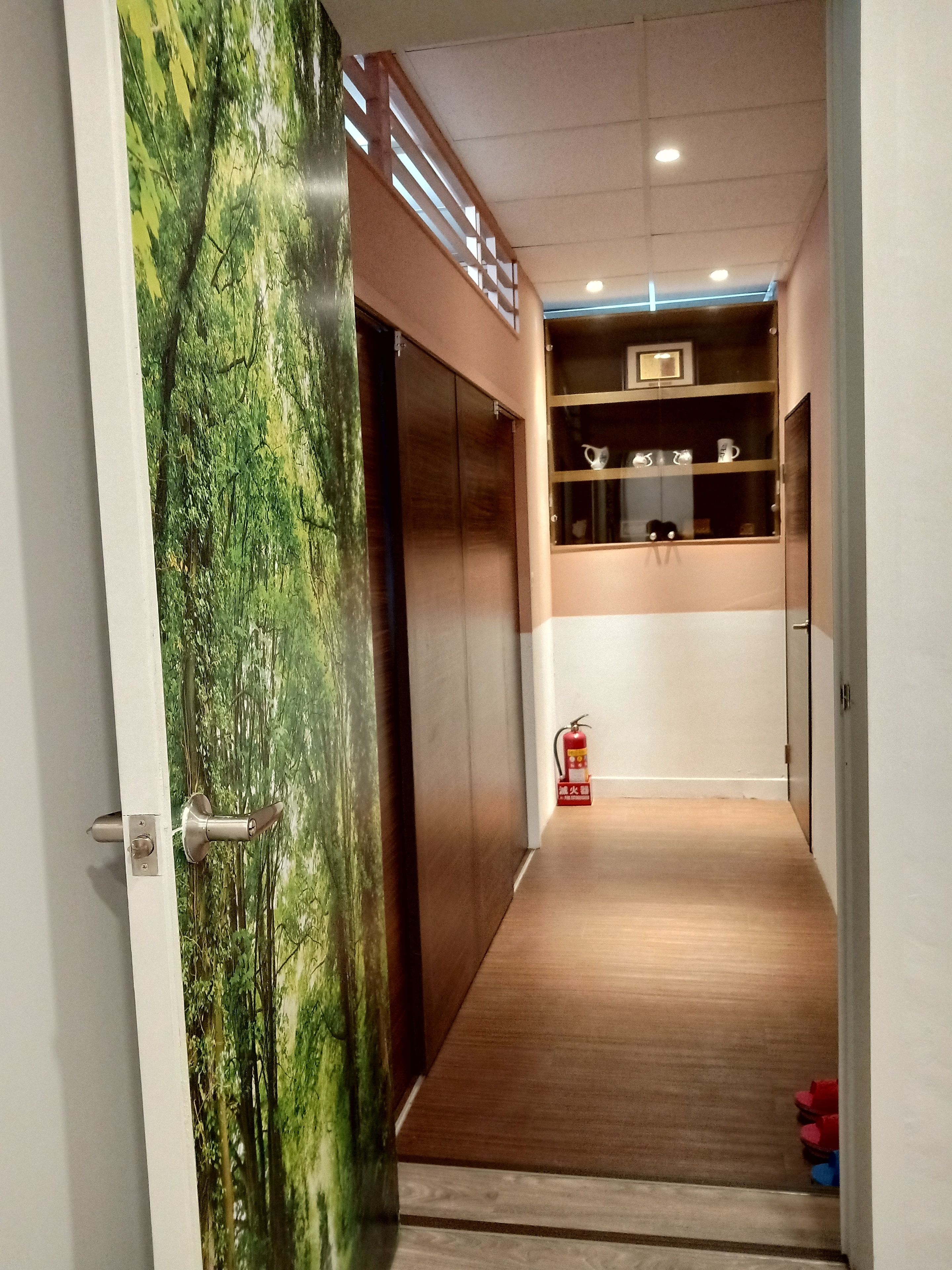 A hallway with a wooden floor, a fire extinguisher, and a shelf with cups.