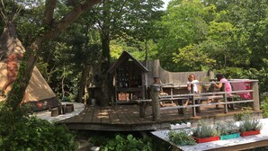 Eine Holzterrasse mit einer rustikalen Holzhütte, umgeben von üppigem Grün und Bäumen.