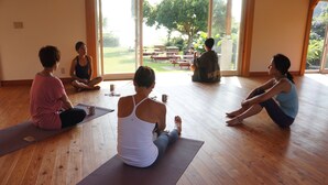 Eine Gruppe von Personen sitzt auf Yogamatten in einem Raum mit Holzböden und großen Fenstern.