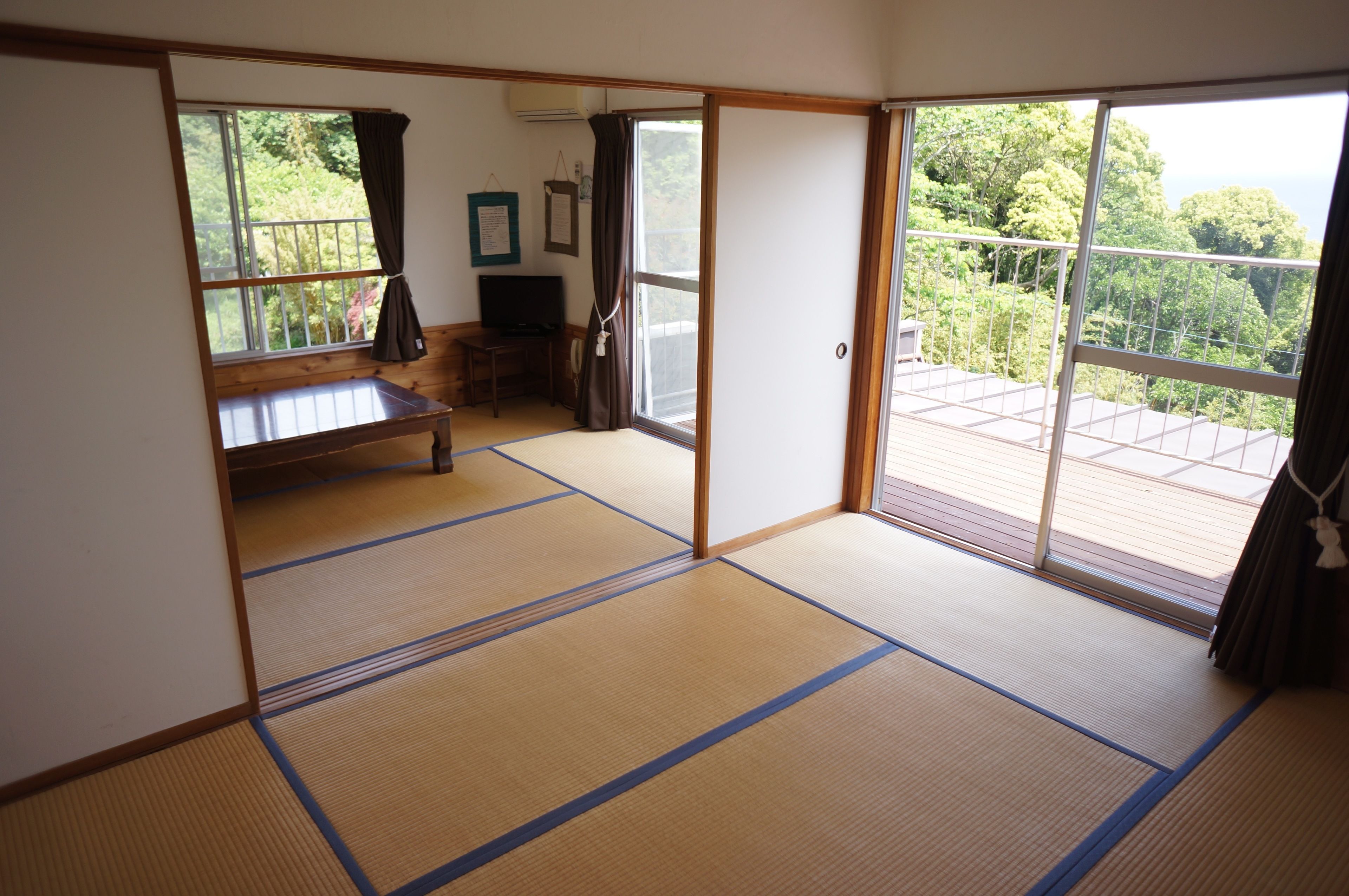 A traditional Japanese room with tatami flooring, a sliding door leading to a balcony, and a television on a wooden cabinet.