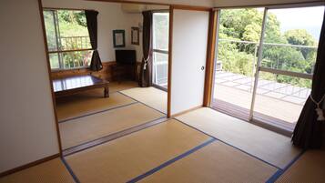 A traditional Japanese room with tatami flooring, a sliding door leading to a balcony, and a television on a wooden cabinet.