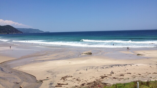 Ein Strand mit blauem Himmel, ruhiger Wellen und ein paar Personen im Wasser.