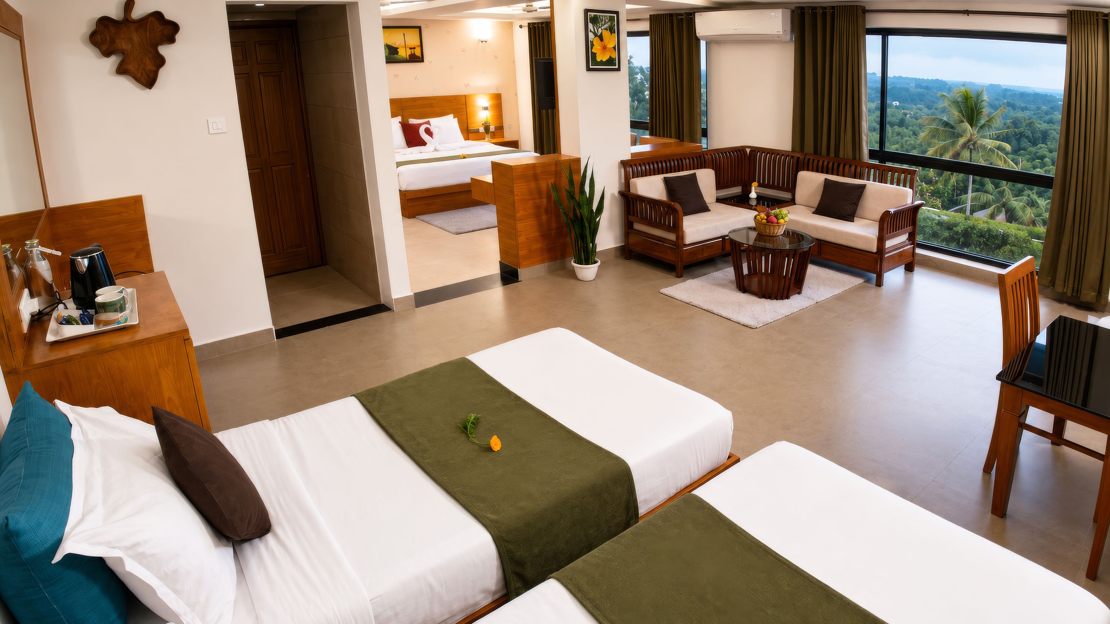 Habitación de hotel con dos camas, una zona de estar con sofá y sillones, una mesa de comedor y vistas al exterior.