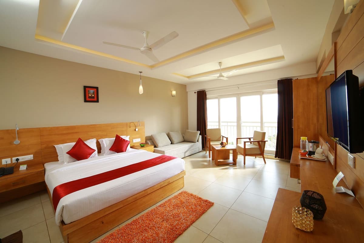 Habitación de hotel con una cama grande, un escritorio con televisor, un sofá y un balcón con vistas.
