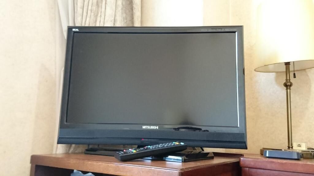 A Mitsubishi flat-screen TV on a wooden stand in a hotel room.