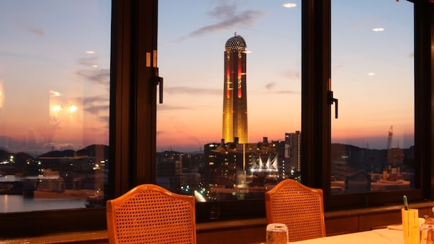 A table set for two with a view of a city skyline at dusk. - Plaza Hotel Shimonoseki (Shimonoseki)