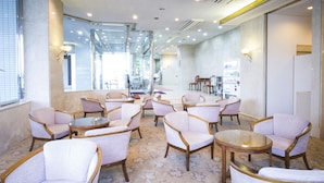 A modern hotel lobby with seating areas, a reception desk, and a view of the street through large windows. - Plaza Hotel Shimonoseki (Shimonoseki)