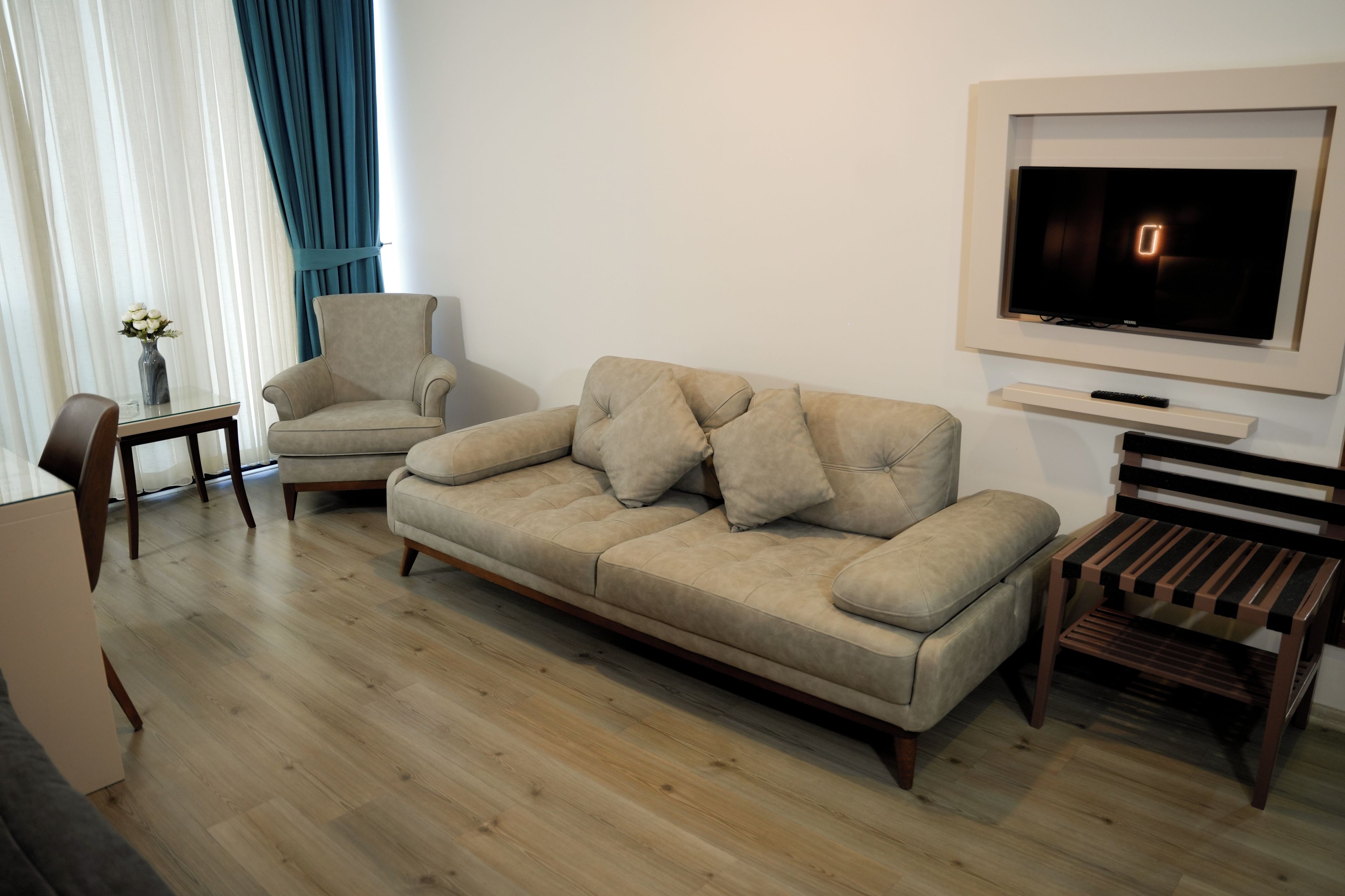 A modern living room with a sofa, armchair, TV, and a small table with a vase.