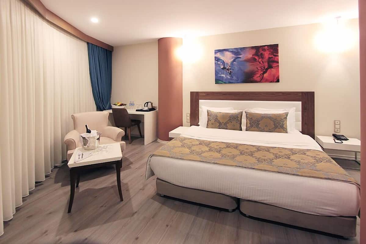 A hotel room with a large bed, a desk, a chair, and a painting on the wall.