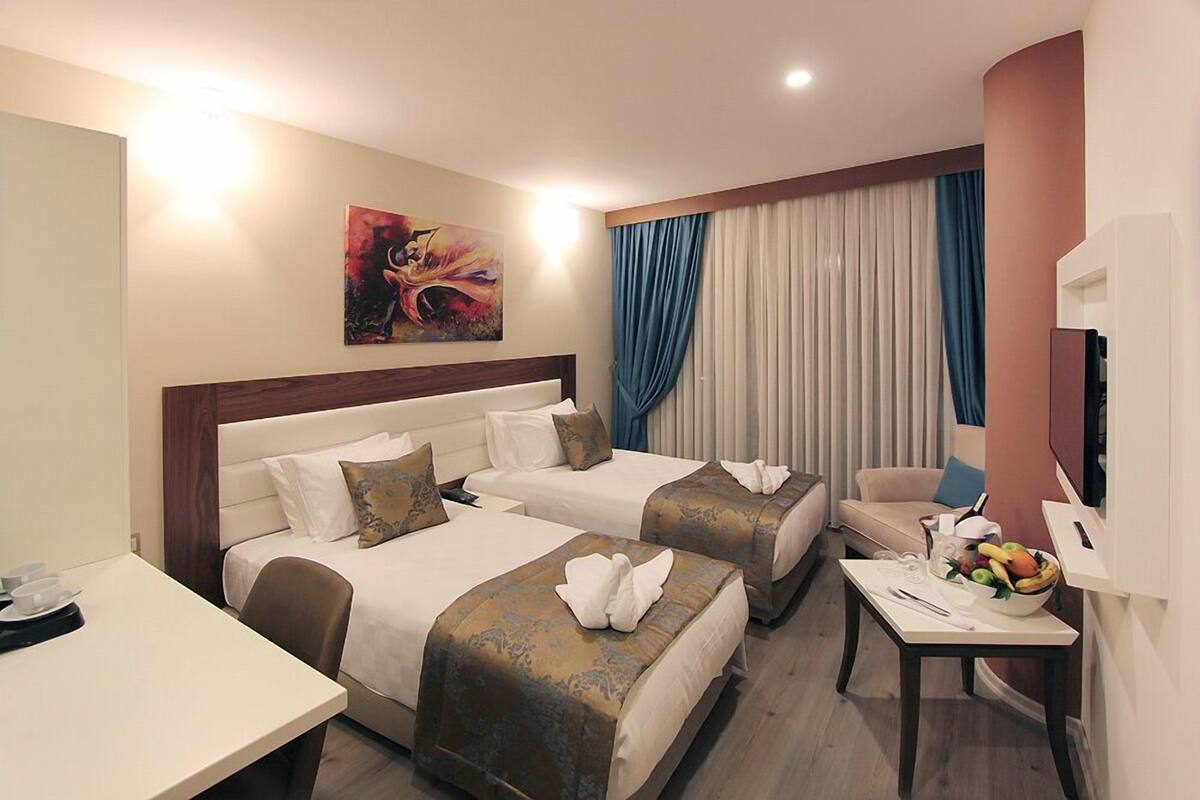 A hotel room with two beds, a desk, a chair, and a TV.