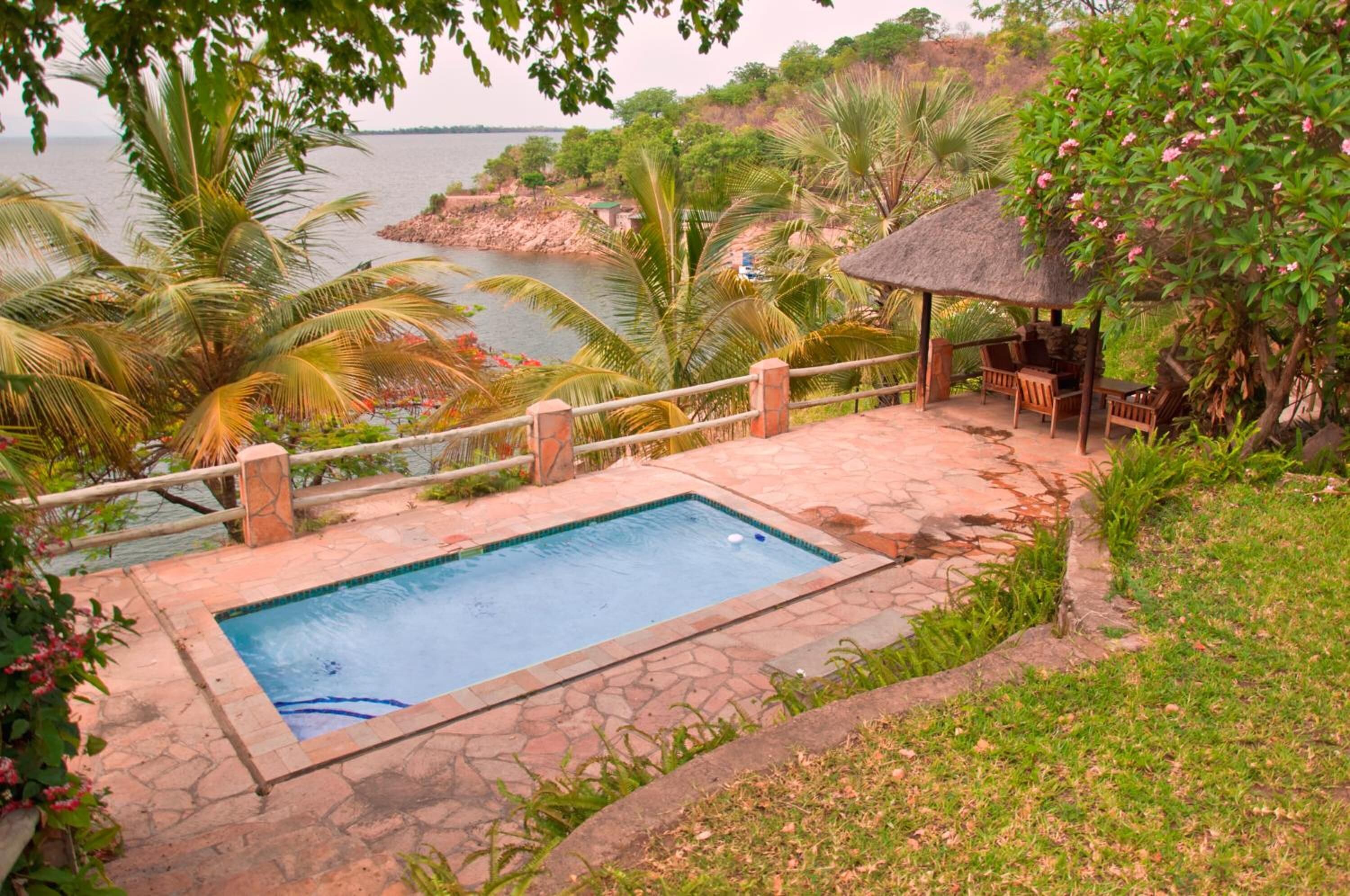 Una piscina con cubierta de piedra, rodeada de palmeras y un quiosco con techo de paja.