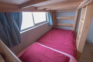 Una habitación pequeña con cama individual, techo de madera y ventana con cortina.
