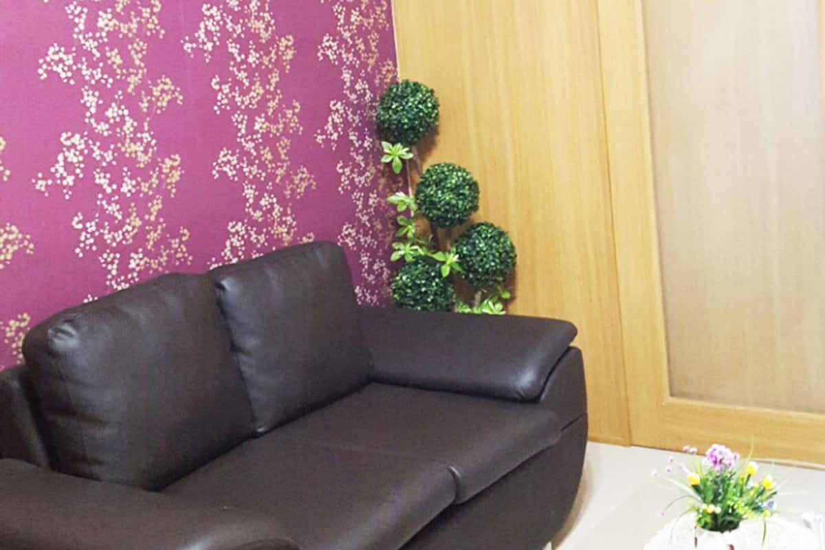 A room with a dark brown leather sofa, a small table with a glass top, a wooden wardrobe, and a purple floral wallpaper.