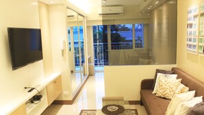 A modern living room with a flat-screen TV, a glass coffee table, and a brown sofa with patterned cushions. - Shell Residences Apartment by Homebound (Pasay)